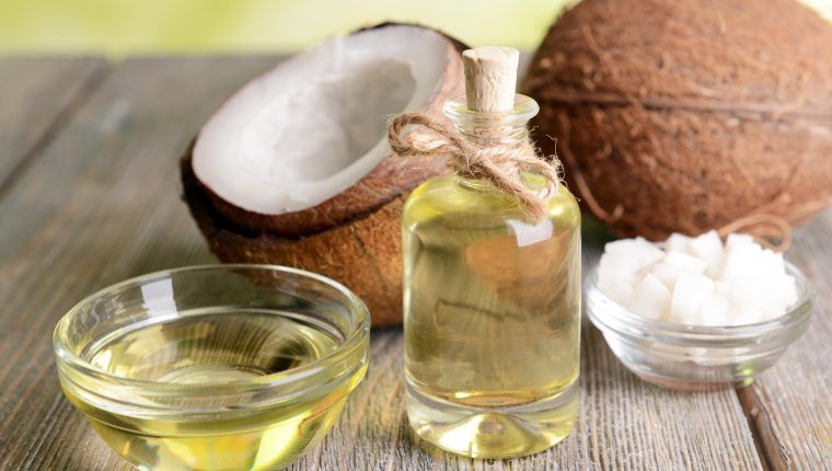 Aceite de coco para piojos en una botella con cuerda, junto a un coco fresco abierto y dos tazones con aceite líquido y coco rallado.